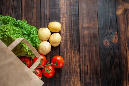 Paper bag on a wooden brown background, vegetables from the store. Tomatoes, salad, potatoes. Empty space for text.の写真素材