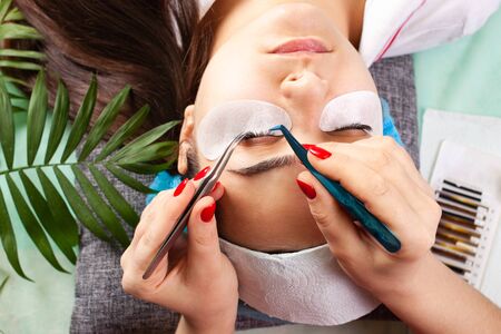 Master increases eyelashes of a young girl in a beauty salon. Professional eyelash extensions. Green...