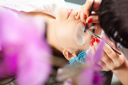 Master increases eyelashes of a young girl in a beauty salon. Professional eyelash extensions. Woman...