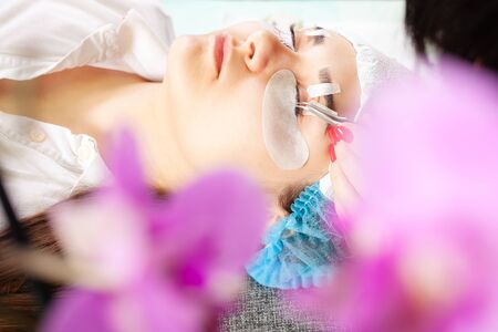 Master increases eyelashes of a young girl in a beauty salon. Professional eyelash extensions. Woman...