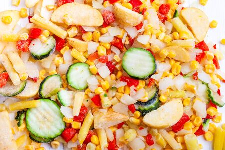 Vegetable frozen mixture for frying. Frozen zucchini, potatoes, corn, beans, peppers, onions on a white wooden background. Quick diet dinner.の写真素材