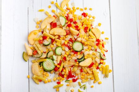 Vegetable frozen mixture for frying. Frozen zucchini, potatoes, corn, beans, peppers, onions on a white wooden background. Quick diet dinner.の写真素材
