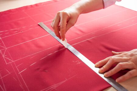 A beautiful seamstress woman in her own atelier makes a pattern on the red fabric. The master is painting the fabric for future clothing. A girl does things with her own hands.の写真素材