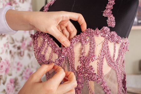 The seamstress sews lace and beads to the pink dress