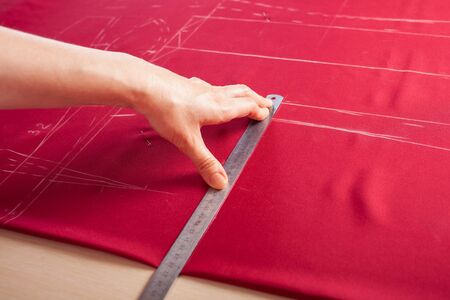 A beautiful seamstress woman in her own atelier makes a pattern on the red fabric. The master is painting the fabric for future clothing. A girl does things with her own hands.の写真素材