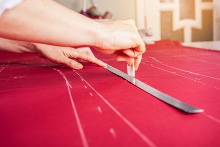 A beautiful seamstress woman in her own atelier makes a pattern on the red fabric. The master is...