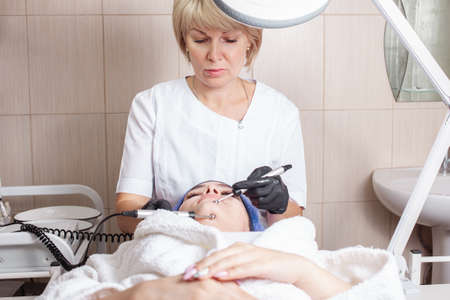 The beautician massages the face in the beauty salon. Improves blood flow, lymph outflow, increases skin elasticity, tones muscles, improves complexion, smooths wrinkles, reduces puffiness.の写真素材