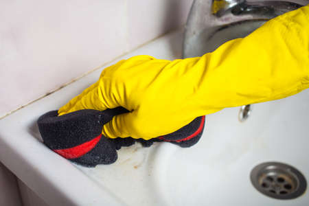 Maid with rubber glove cleaning tap and sink. Housekeeping scrubbing and polishing silver tap in bathroom.の写真素材