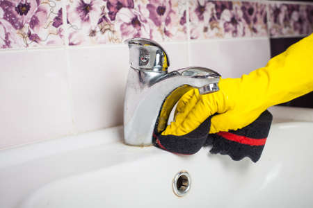 Maid with rubber glove cleaning tap and sink. Housekeeping scrubbing and polishing silver tap in bathroom.の写真素材