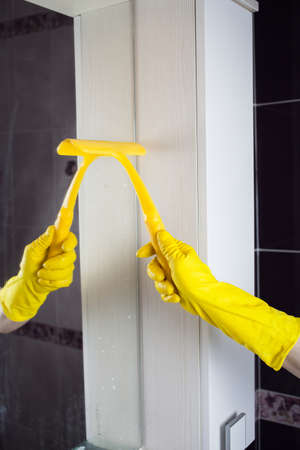 Maid with rubber glove cleaning tap and sink. Housekeeping scrubbing and polishing silver tap in bathroom.の写真素材