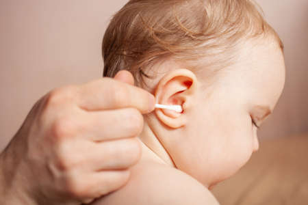 father hand carefully using stick of cotton swab for ears cleaning. Daily baby hygiene. Closeup.