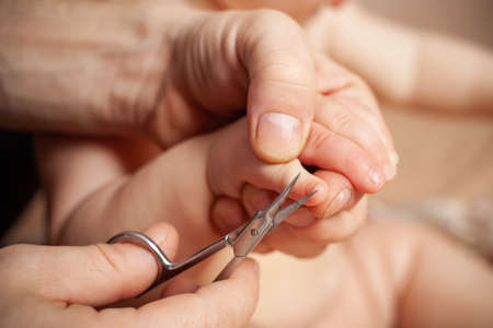 A woman cuts her nails child hygiene. Women's hands hold nail scissors and a child's hand. manicure for baby by hand with scissors to cut the nail for clean with love and care. Space for textの写真素材