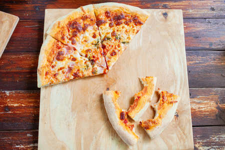 Pizza on a wooden tray. Dry crusts of the edge of the pizza bitten lie nearby. The man didn't finish...