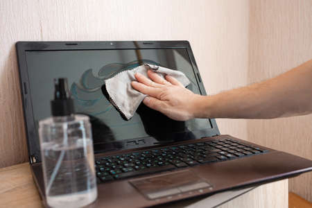 The woman cleans the laptop from dust and bacteria with alcohol spray and rags. Disinfection,...
