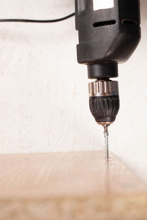 A man drills a hole in the cupboard with a drill. A Euro-shunup, screw-screed for a wood chip slab.