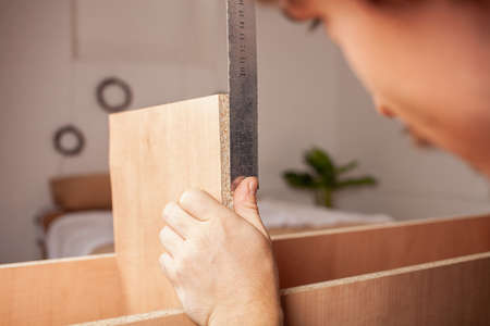 A man measures a ruler shelf for a cabinet of wood shavings.の写真素材