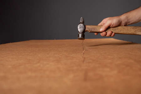 A man hammers nails into a cupboard. The back wall of the cupboard is made of thick cardboard....