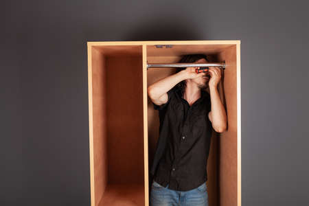 A man twists a pipe for a hanger in a closet with a screwdriver. The crossbar to hang clothes.の写真素材