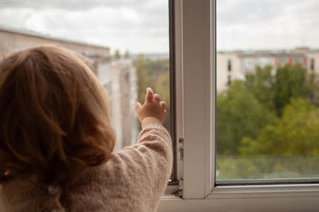 The child climbs to the window, the girl on the window sill rests on the net, the danger of falling....