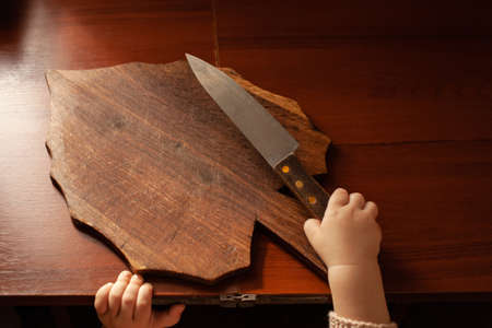 The child pulls a knife from the table, danger. The child can cut, children's home dangers. A little one-year-old girl with a knife.の写真素材