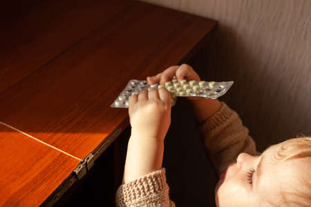 The child took out pills, the girl is playing with medical medicine, a one-year-old child can eat pills and not wake up, poison. Danger in the house, medicines are dangerous for young children.の写真素材