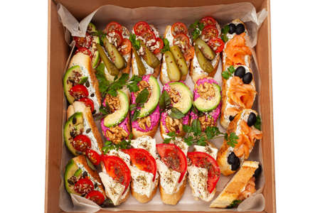 Delivery of food in a box, delicious and fresh food. Convenient boxing for eating at home, at work, in nature. Bruschetta with salmon, cheese, beetroot, nuts, cucumbersの写真素材