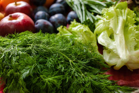 Fruits, vegetables and greens lie on the table, natural light from the window.
