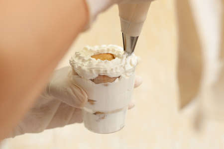 The pastry chef decorates the tiramisu in a glass with whipped cream. Natural light from the window