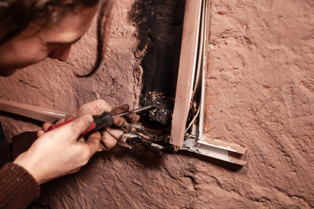 A man fixes a burnt socket. Short circuit, burnt wires. traces of smoke and fire on the wall. The...