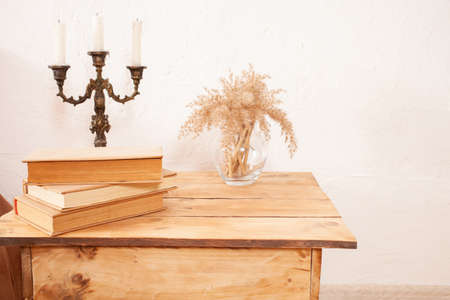 Beige interior, brown books, pampas in a glass vase, candlestick. A wooden bedside table. copy space...