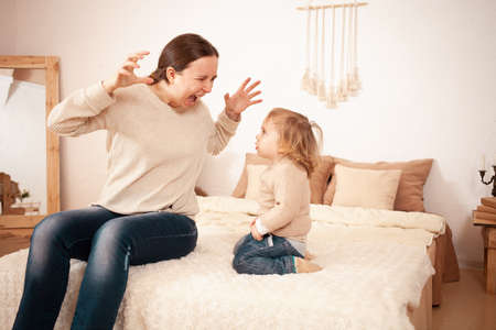 Mom yells Screams angry at baby. A two-year-old girl is afraid of her mother. The woman is nervous and takes out the anger. Family quarrel, innocent child, nerves. Beige home interiorの写真素材