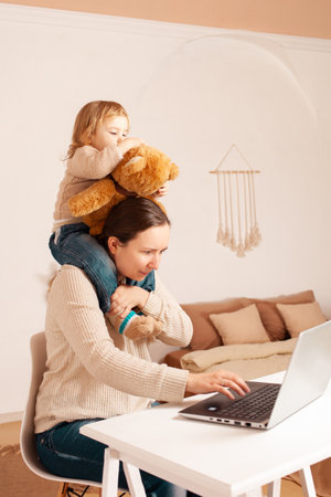 mother works at home for a laptop. The child Prevents the work. A young woman is freelance with her daughter on the computer. interior.の写真素材