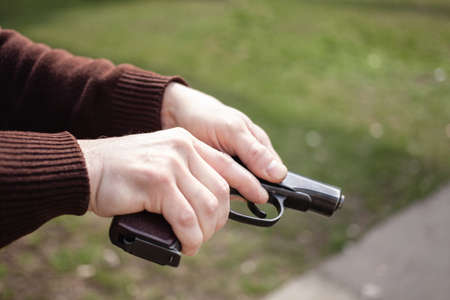 A young man charges a gun against a green grass. Firearms gun outdoor. Sport, hobbiesの写真素材