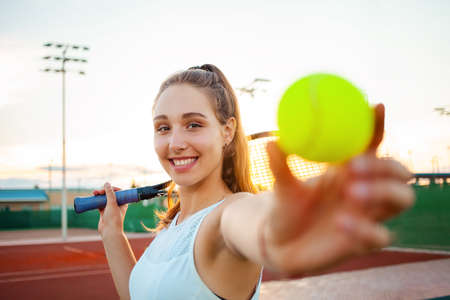 A beautiful woman plays tennis. Sports racket, the girl smiles, happy. Active lifestyle, outdoor recreation. Fitness body, weight loss, rest training. An athlete with a ball in hand loves sportsの写真素材