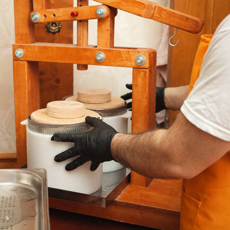 The cheesemaker puts cheese under press, whey. Home production, business, portrait. Wooden...