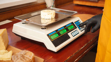 The cheesemaker weighs cheese on scales, home production, business. shopの写真素材