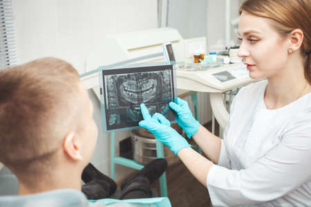 woman doctor shows patient his x-ray of teeth and explains problems. Gloves