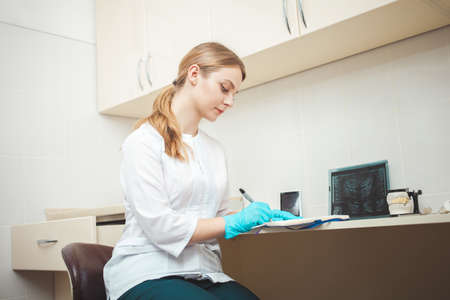 beautiful woman dentist in office, in clinic, indoor. Portrait, smiling and happy. Friendly doctor. makes recordings with penの写真素材