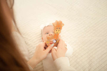 child lies on bed, plays with toy, mother teaches her daughter, newborn baby in bedroom. Wooden toy...