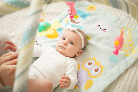 child lies on bed, hanging toys, baby mat, newborn girl. developing, watching toys, satisfied. cute...