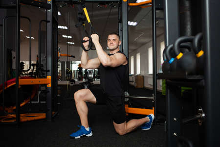 A beautiful trainer performs exercises on the simulator, squats, push-ups on weight, muscular body....