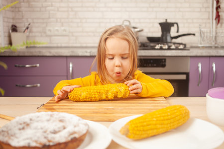 funny girl eats corn, indulges, lavender kitchen in background. wrigglesの写真素材