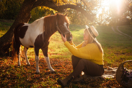 woman and spotted brown pony at sunset in forest, beautiful girl in autumn clothes loves her horse, concept of kindness, animal care, nature and friendship. hatの写真素材