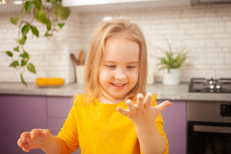three-year-old girl in yellow jacket is preparing to cook food in the kitchen. Portrait of happy child. hand in flourの写真素材