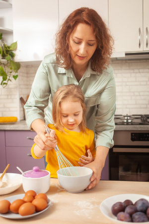 Mother and daughter cook pie in purple kitchen, training and development, interesting game and help. Happy family together.の写真素材