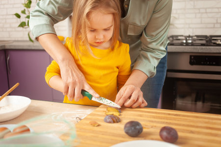 Mother and daughter cook pie in purple kitchen, training and development, interesting game and help. Happy family together. cut fruitの写真素材