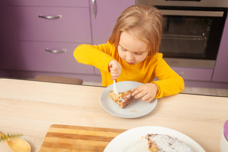 funny little girl eats plum pie with sugar, happy and satisfied, holding spoon on her own. morselの写真素材