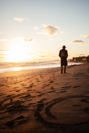 Beach solitude man walks under warm sunset glow.の写真素材