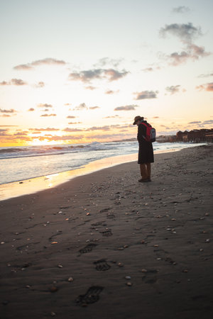 Gentle waves lap as man walks seaside at twilightの写真素材