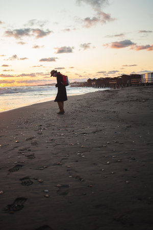 Silhouetted figure walks along sandy shore at duskの写真素材
